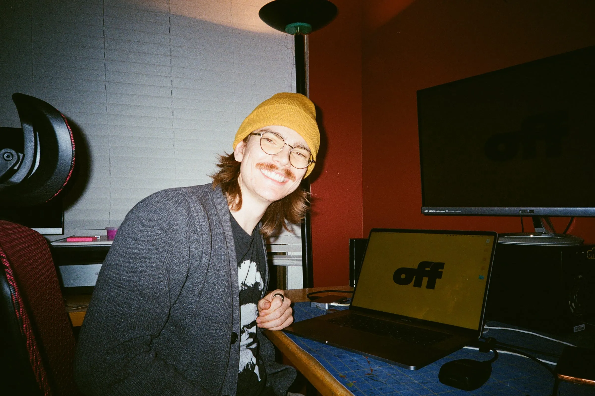 Edward Pollei smiling at his desk in a yellow beanie — self-portrait on film