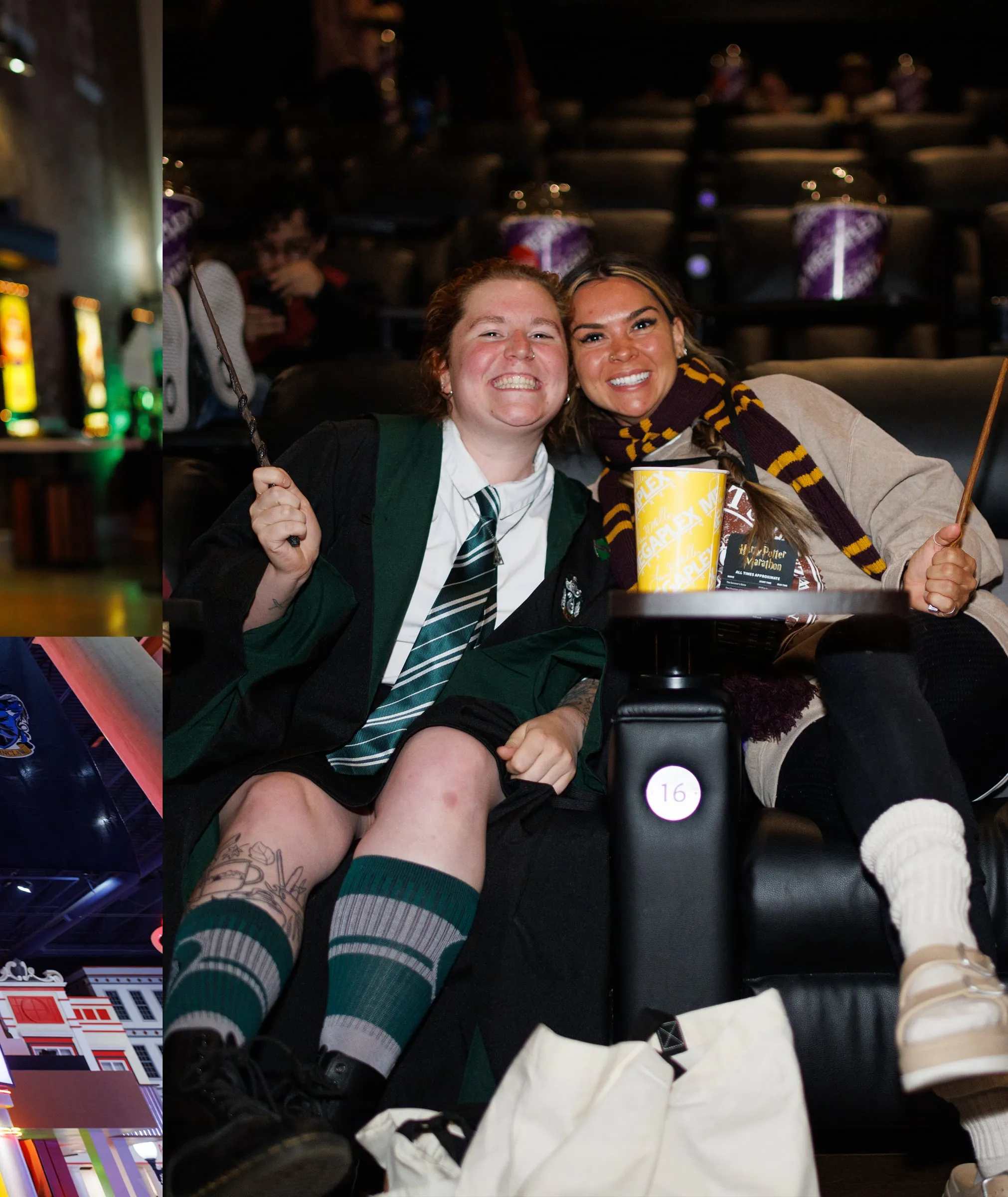 Two fans in house robes grinning with wands raised in a theater