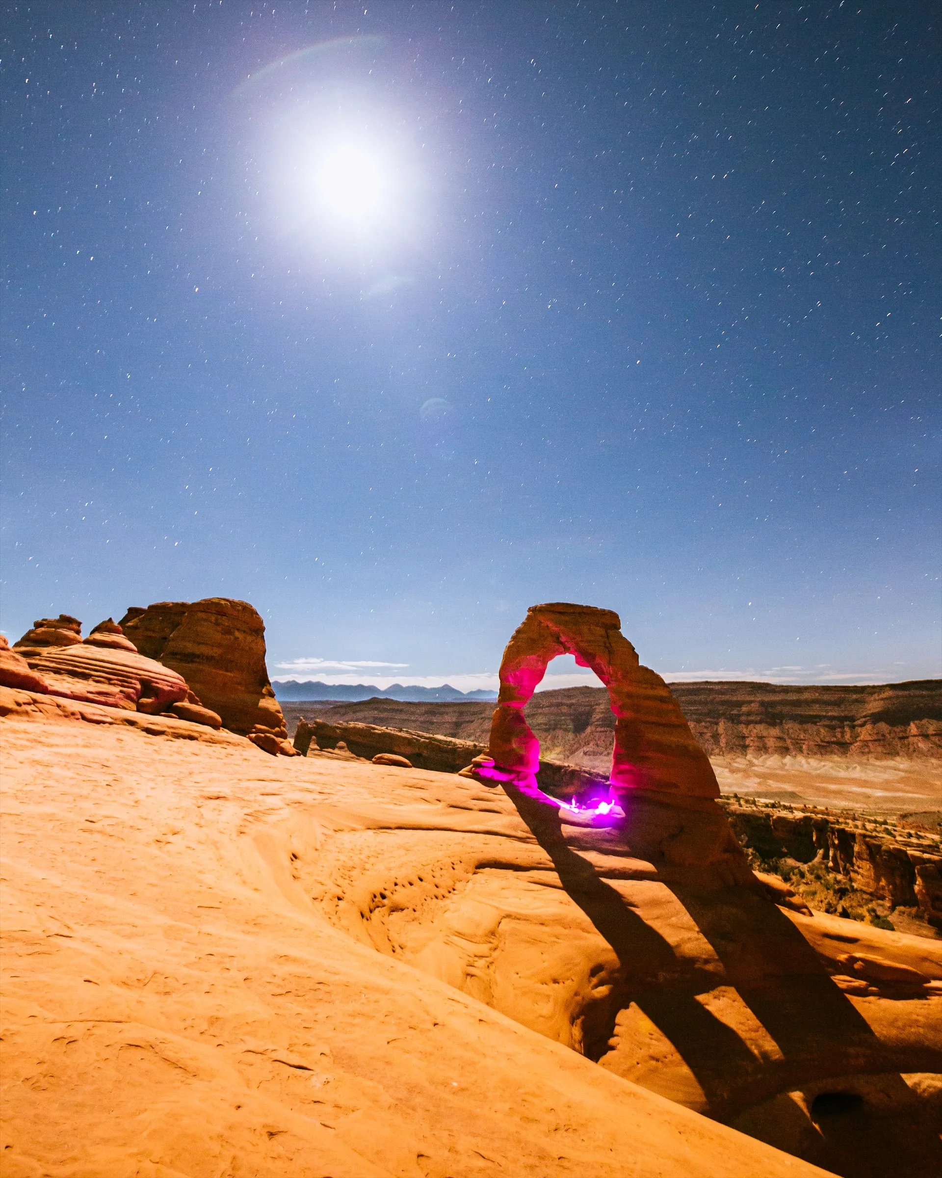 Delicate Arch under a full moon with a pulse of magenta light inside the arch
