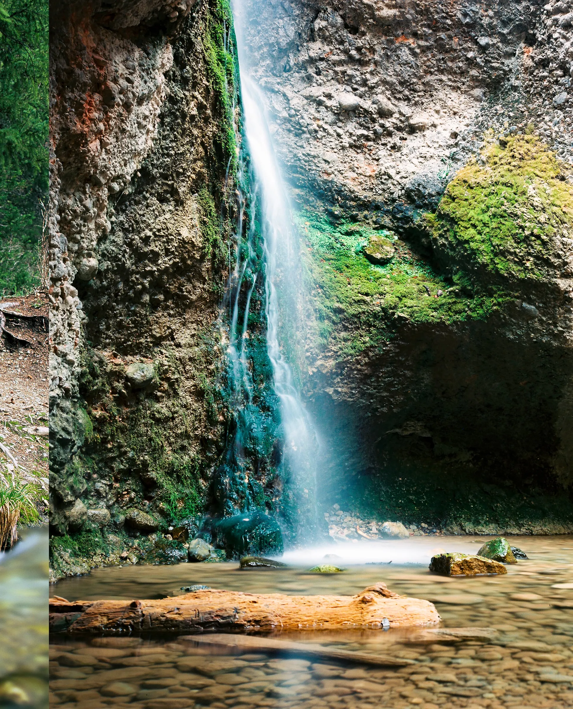 Thin waterfall dropping past mossy rock into a shallow pool