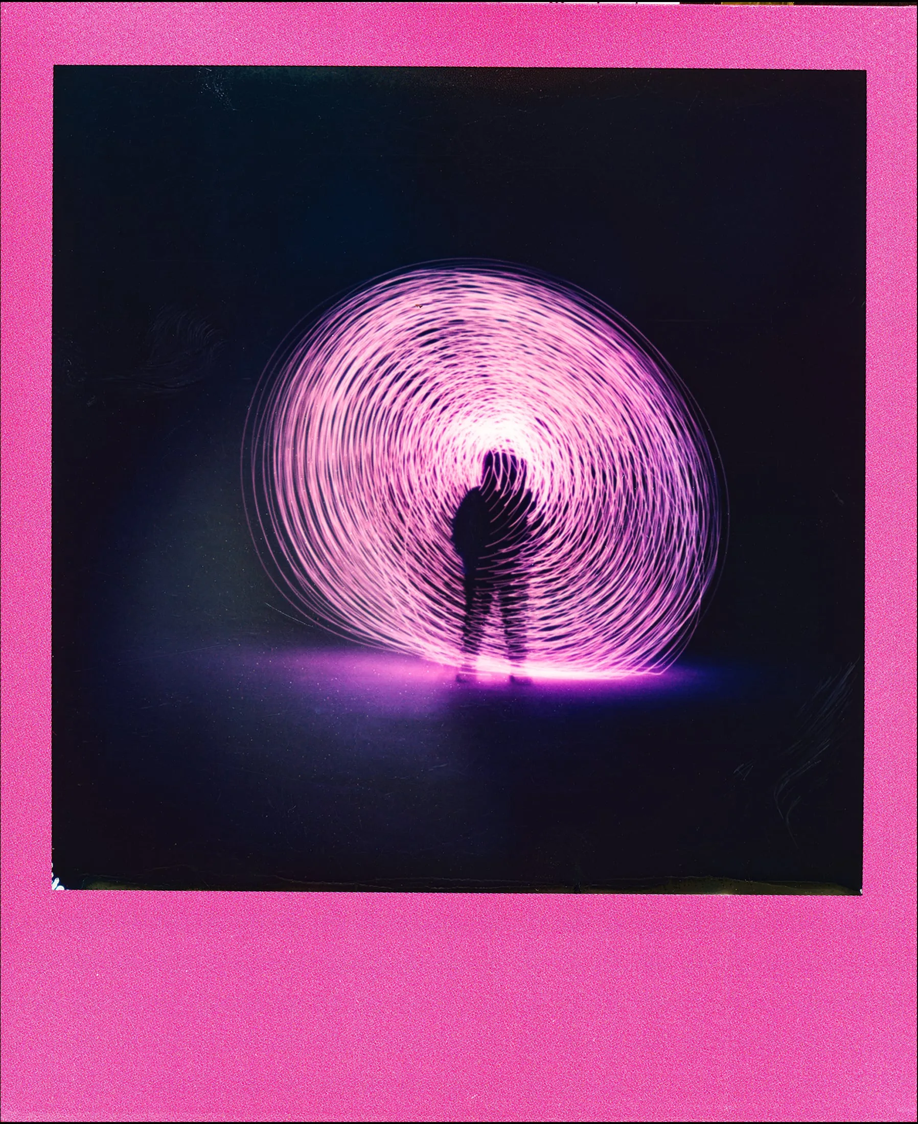 Pink-framed Polaroid of a figure inside a spiral of spun light
