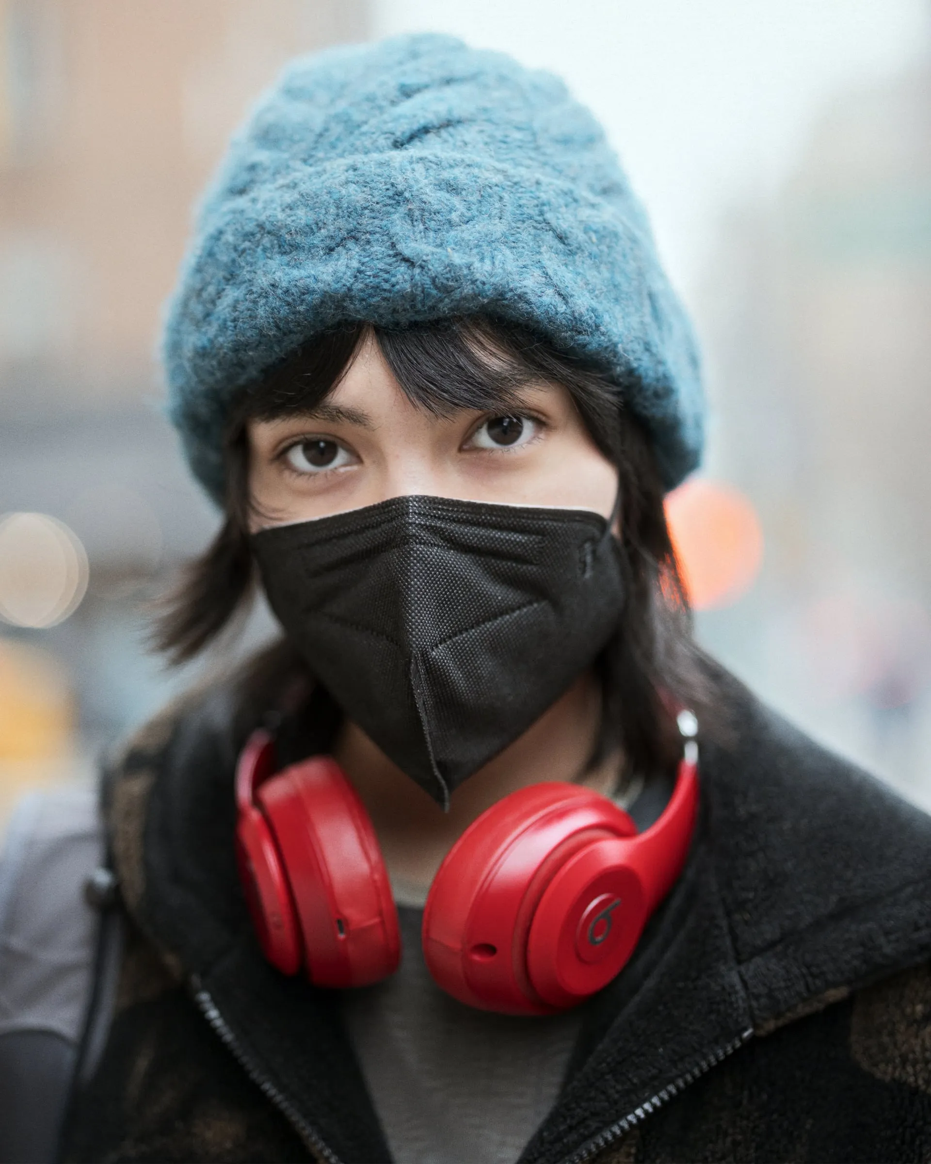 Street portrait of a woman in a blue beanie, black mask, and red headphones