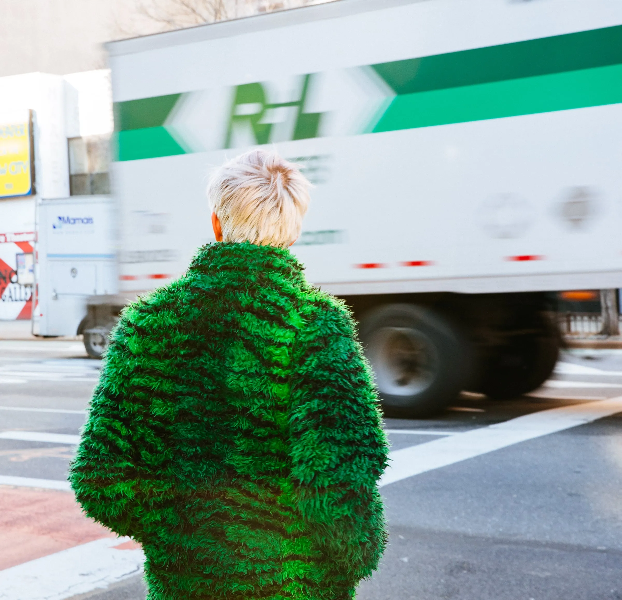 Figure in a shaggy green coat watching a truck blur past